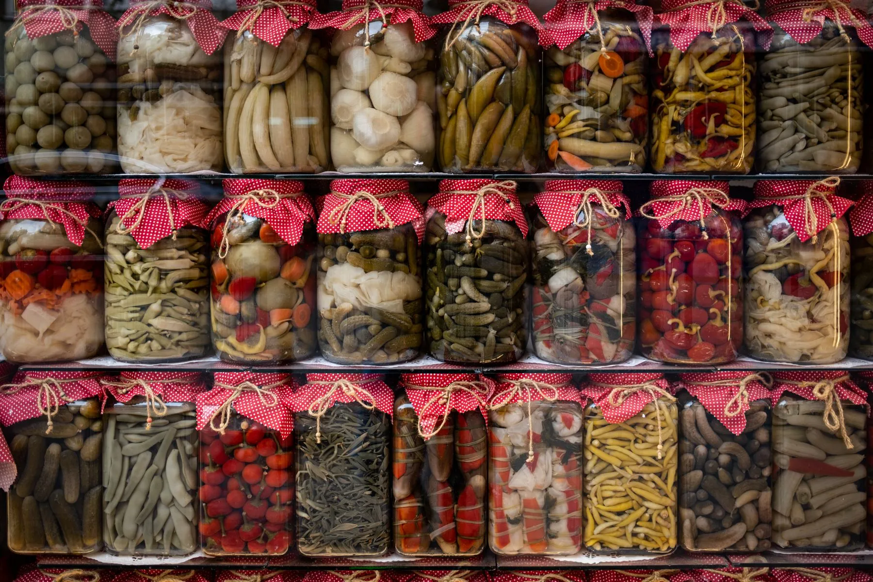 Glass jars of fermented pickles filled with cucumber, tomato and garlic on display
