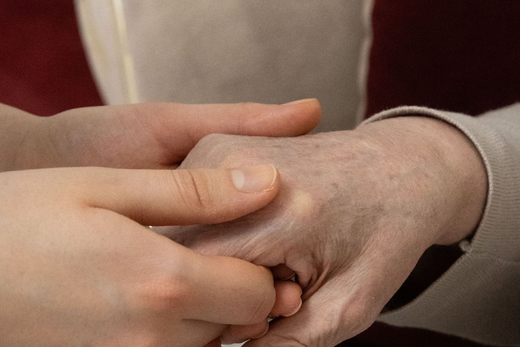 椅子に座る高齢の家族の手を若い人が両手で支えている様子