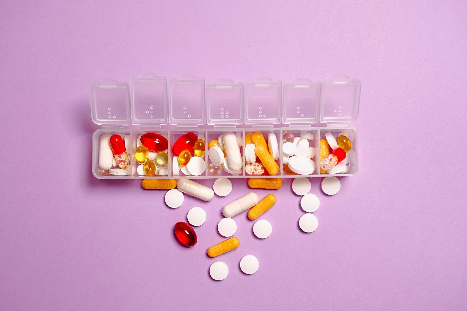 Stock photo of a weekly pill organizer and tablets on a purple background