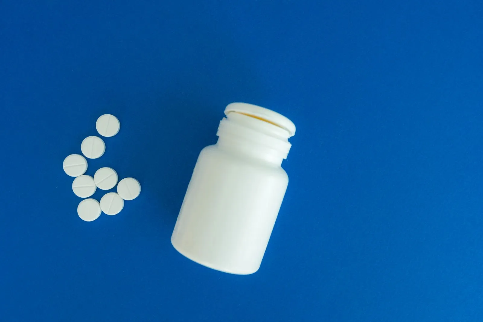 A white pill container and tablets on a blue background