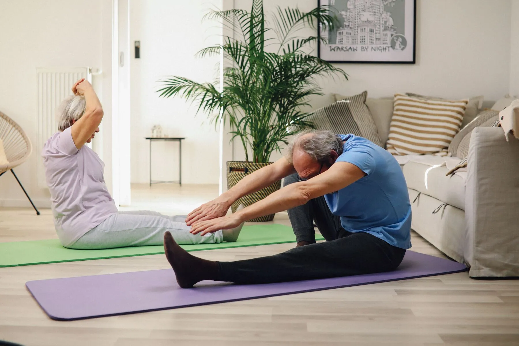Two older adults stretching on exercise mats in a living room